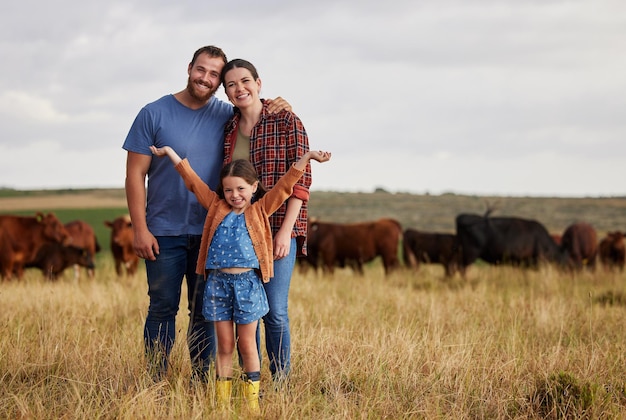 Familia feliz de pie en una vaca de granja en el fondo y con una visión de crecimiento en el retrato de la industria Pareja de campo o granjero en un campo de ganado de pasto y animales de ganado de campo libre