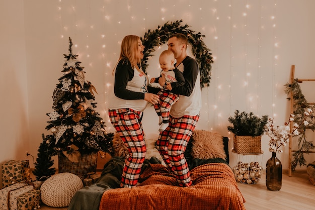 Familia feliz en pijama con los padres juegan con el niño saltando en la cama en el dormitorio. ropa familiar de año nuevo se ve trajes. Regalos de celebración del día de San Valentín