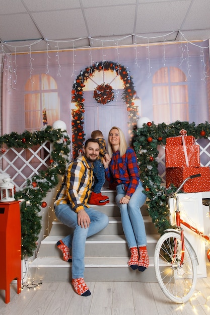 Família feliz posando em uma varanda decorativa. Festa de Natal em casa. Mamãe, papai e filho usavam roupas casuais. Família feliz engraçada brincando na casa deles. Decoração de Natal no interior da casa