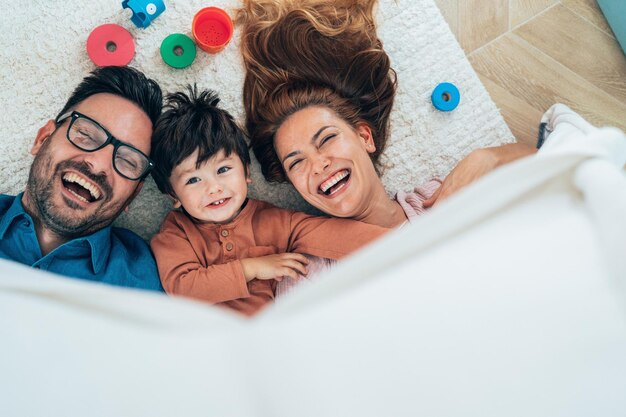 Foto família feliz posando sob um edredão enquanto olha para a câmera