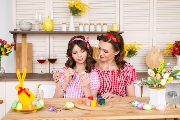 La familia feliz se prepara para la Pascua Mamá mira a su hija decorar los huevos de Pascua