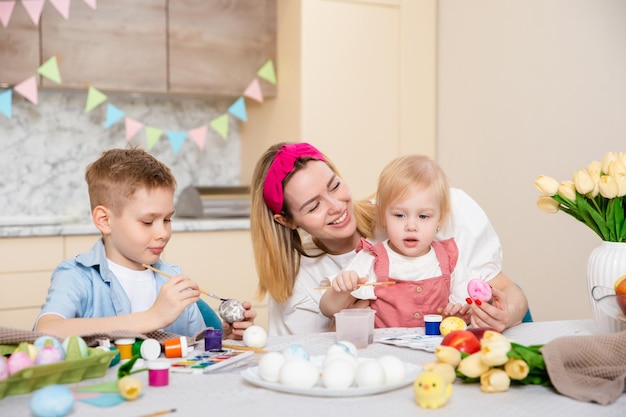 Familia feliz preparándose para Pascua Niños lindos con madre pintando huevos Actividad en el hogar Concepto de unidad y amor Mamá hijo hija Hermano y hermana