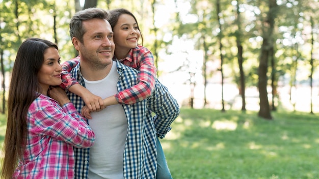 Familia feliz que lleva la camisa a cuadros del modelo que se coloca en el parque que mira lejos