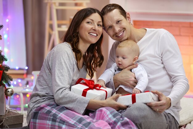 Familia feliz con regalos contra chimenea decorada en la habitación