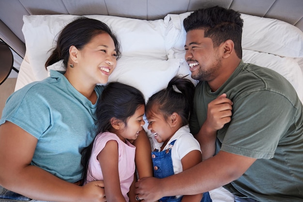 Família feliz relaxa na cama em casa de cima e se une no quarto Conforto do sono e descanso da mãe indiana carinhosa, pai e filhos ou meninas sorriem deitados em lençóis aconchegantes e brincando em casa