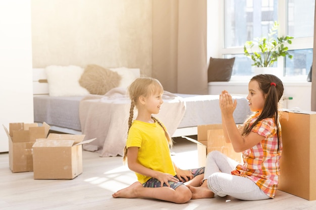 Familia feliz en la sala de estar. Hijas preescolares sentadas y ayudando a desempacar cajas de cartón. Comprar bienes raíces, reubicación en casa nueva y moderna
