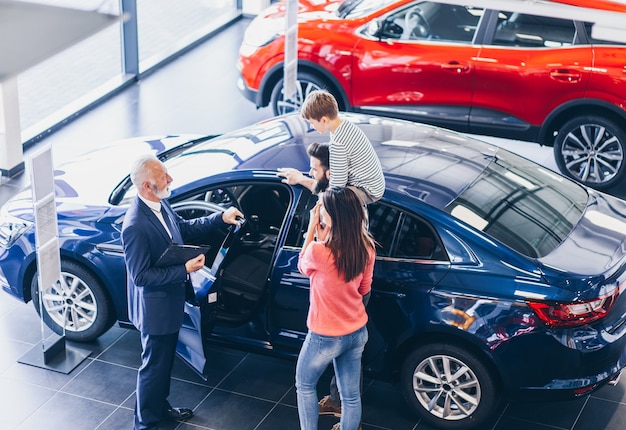 Familia feliz en la sala de exposición de automóviles eligiendo un nuevo para comprar.