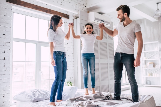 La familia feliz saltando en la cama