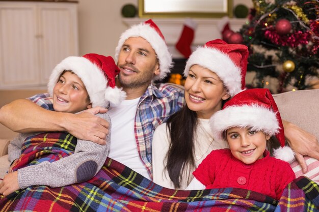 Familia feliz en santa sombrero abrazándose bajo la cubierta