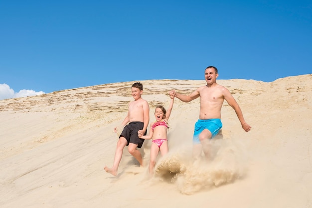 Família feliz se diverte correndo ao longo da praia. Jogos de esportes familiares ao ar livre