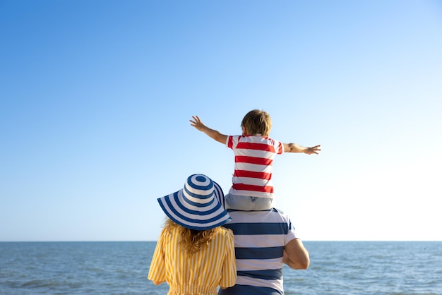 Família feliz se divertindo na praia Mãe pai e filho contra o fundo azul do mar e do céu Conceito de férias de verão Retrato de vista traseira