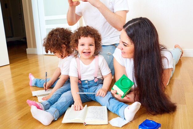 Foto família feliz se divertindo no chão na sala mãe pai e filha menina rindo brincando escrevendo em um caderno