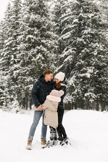 Família feliz se divertir na floresta de inverno. Mãe, pai e filha brincando com a neve. Conceito de família