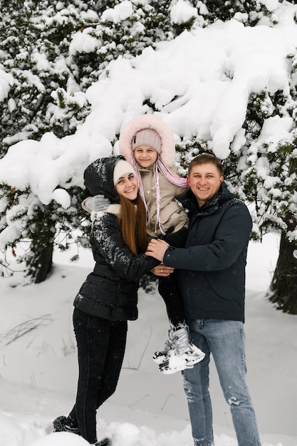 Família feliz se divertir na floresta de inverno. Mãe, pai e filha brincando com neve. Gostando de passar algum tempo juntos. Conceito de familia