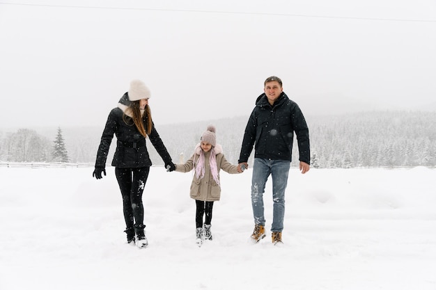 Família feliz se divertir na floresta de inverno. Mãe, pai e filha brincando com neve. Gostando de passar algum tempo juntos. Conceito de familia