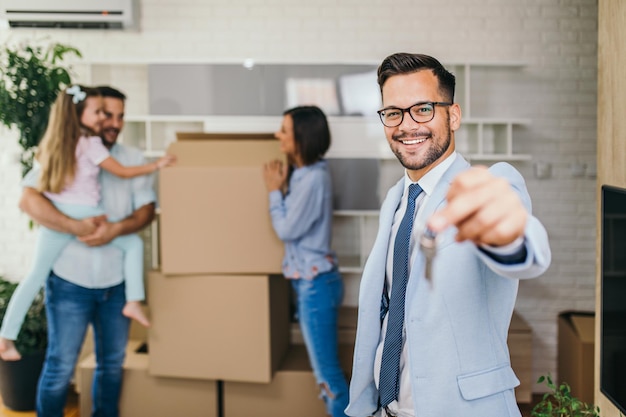 Família feliz se mudando para sua nova casa. Agente imobiliário mostrando as chaves do apartamento e sorrindo.