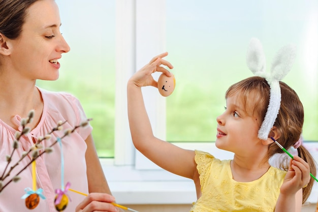 Família feliz se preparando para a Páscoa garotinha usando orelhas de coelho e mostra sua mãe pintou ovo