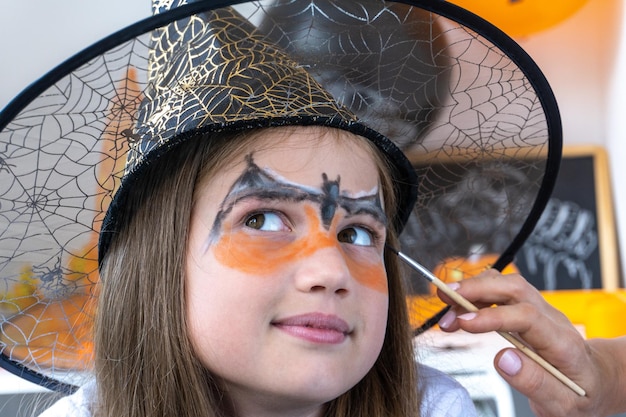 Família feliz se preparando para o Halloween. Mãe desenha maquiagem aqua no rosto de menina para festa de férias