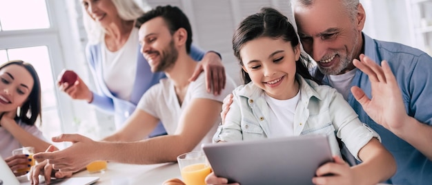 La familia feliz sentada con una computadora portátil y la tableta en la mesa