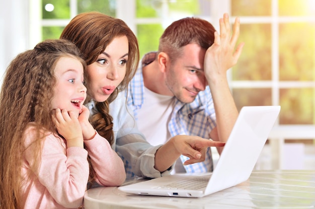 Familia feliz sentada a la mesa con laptop