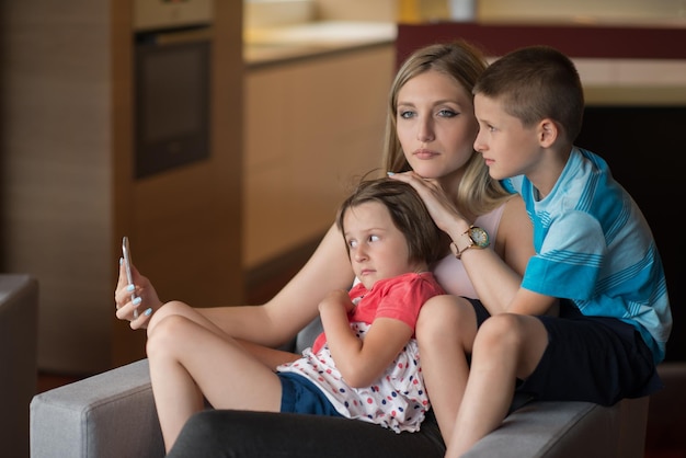 Familia feliz sentada en el sofá y usando el teléfono celular para videollamadas en casa