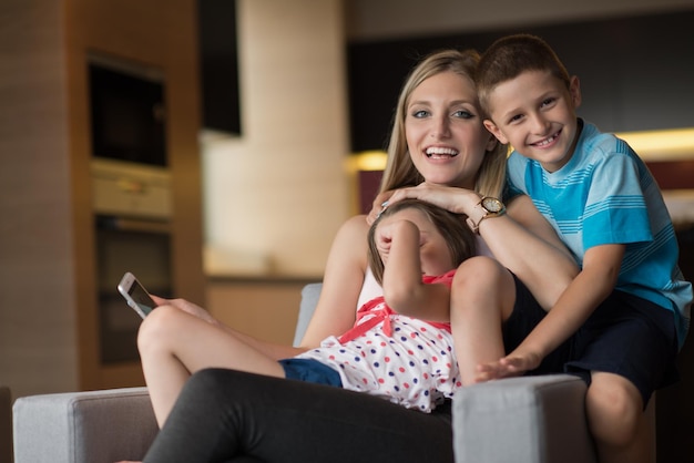 Familia feliz sentada en el sofá y usando el teléfono celular para videollamadas en casa