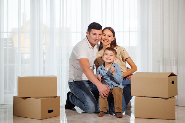 Familia feliz sentada en el suelo de su nueva casa entre cajas de cartón.