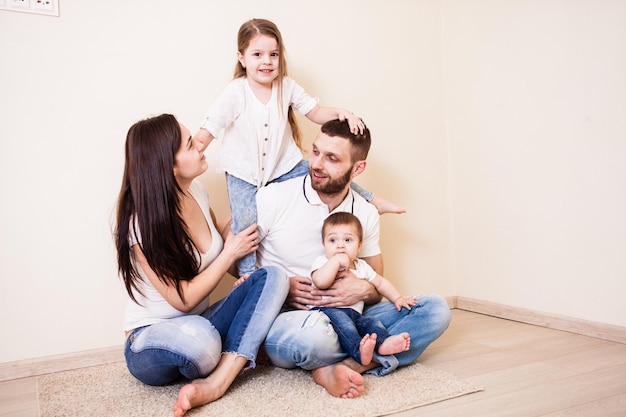 Familia feliz sentada en el suelo con el telón de fondo de una pared blanca