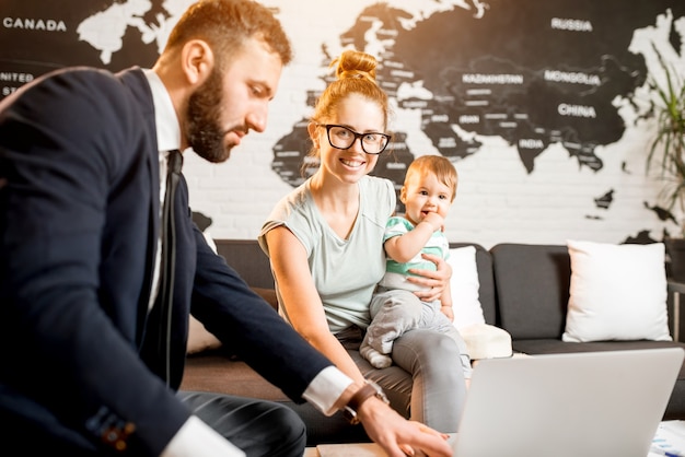 Familia feliz sentado con el agente del hombre en la oficina de la agencia de viajes con un hermoso mapa en el fondo eligiendo un recorrido para unas vacaciones de verano