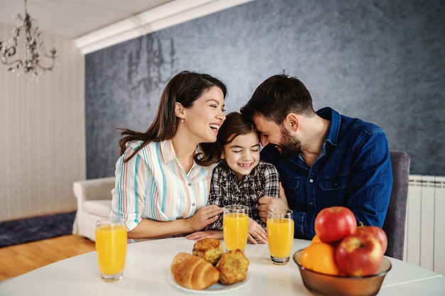 Família feliz sentados juntos à mesa de jantar pela manhã. mamãe e papai abraçando seu único filho.