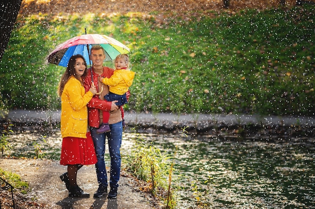 Família feliz sob o guarda-chuva se esconder da chuva.