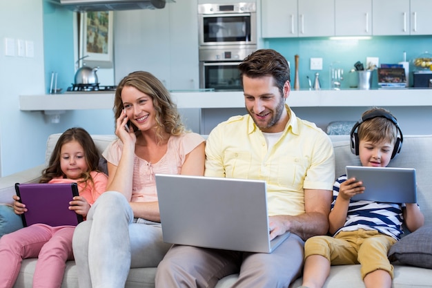 Familia feliz en el sofá junto usando dispositivos