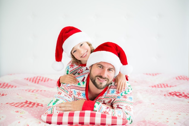 Familia feliz con sombreros de Santa Claus acostado en la cama, el padre y el niño se divierten en Navidad