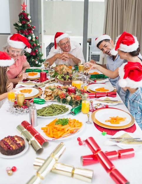 Familia feliz en sombreros de santas disfrutando de la cena de Navidad