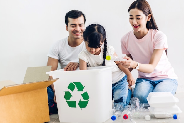 Foto familia feliz y sonriente divirtiéndose poniendo botellas de plástico y papel vacíos en la caja de reciclaje