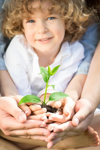 Familia feliz sosteniendo planta joven verde en primavera al aire libre Concepto de ecología