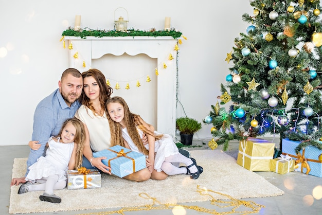 La familia feliz sostiene cajas con regalos frente a una chimenea blanca con un elegante árbol de Navidad