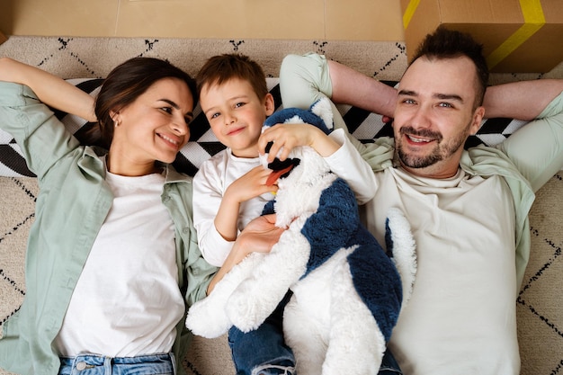 Familia feliz tirada en el suelo en un nuevo hogar con cajas de cartón alrededor