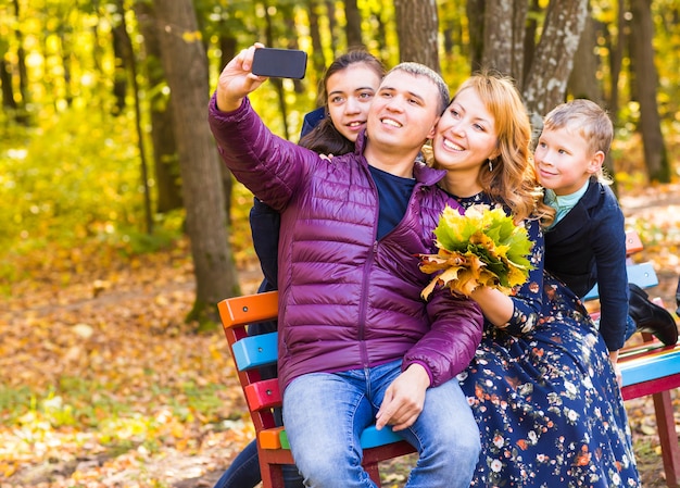 Família feliz tirando selfie com smartphone no parque outonal