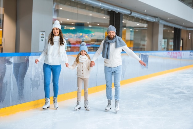 familia feliz tomados de la mano mientras patinan juntos en la pista de hielo