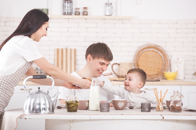 Família feliz tomando café juntos. família jovem comendo à mesa na cozinha. mãe, pai e bebê comendo.