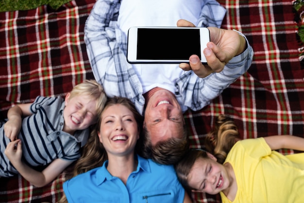 Familia feliz tomando una selfie mientras está acostado en el parque