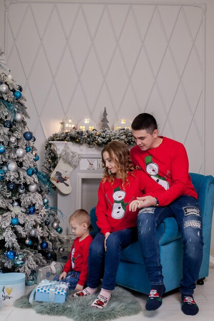 Familia feliz de tres madres jóvenes que esperan un nuevo bebé padre y su pequeño hijo cerca del árbol de Navidad decorado