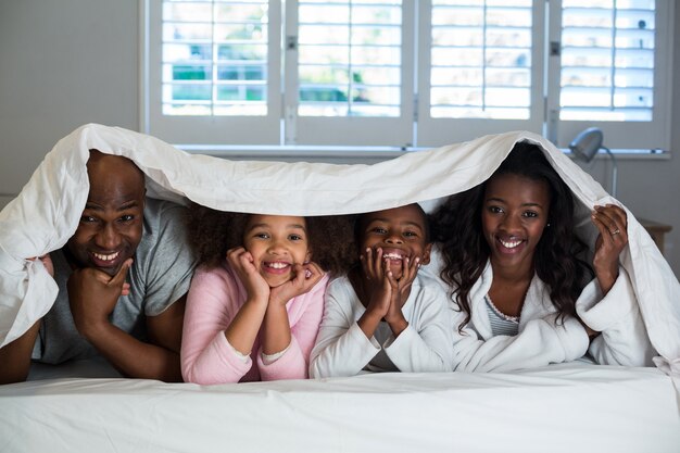 Familia feliz tumbado debajo de una manta en la cama