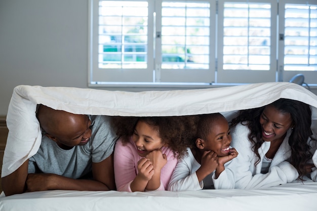 Familia feliz tumbado debajo de una manta en la cama