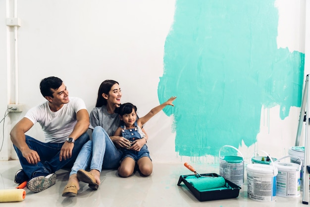 Família feliz usando um rolo de pintura e paredes de pintura em sua nova casa
