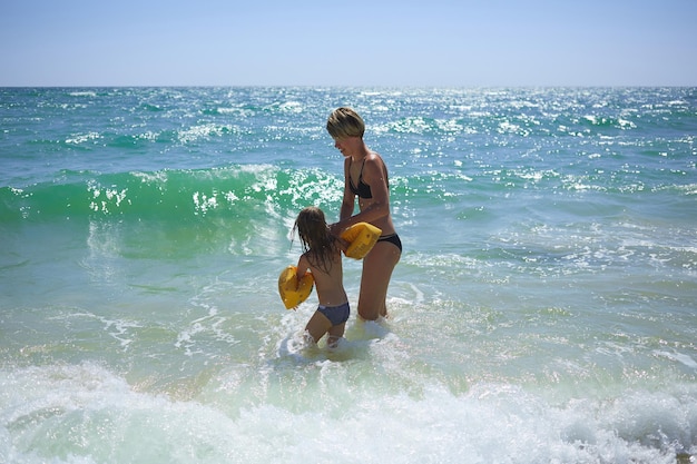 Familia feliz de verano de niño rubio de seis años jugando y saltando olas de agua abrazando a la madre de la mujer en la playa de la orilla del mar