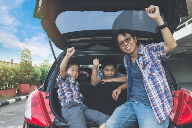 Familia feliz en un viaje por carretera, sentado en el maletero del coche