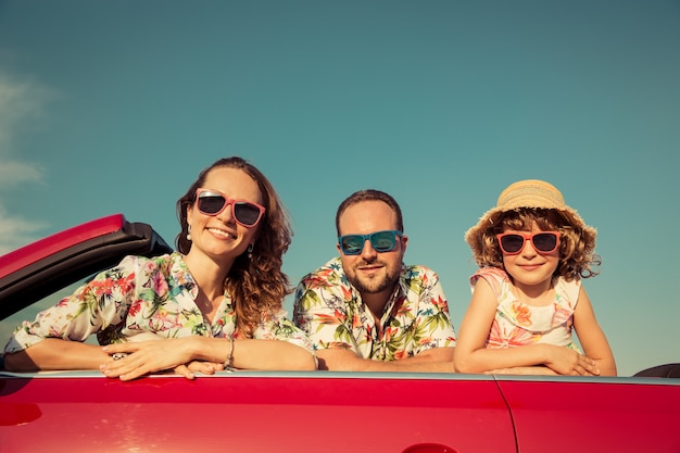 Familia feliz viaje en coche en las montañas Gente divirtiéndose en cabriolet rojo Concepto de vacaciones de verano