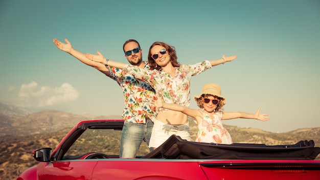 Familia feliz viaje en coche en las montañas Gente divirtiéndose en cabriolet rojo Concepto de vacaciones de verano